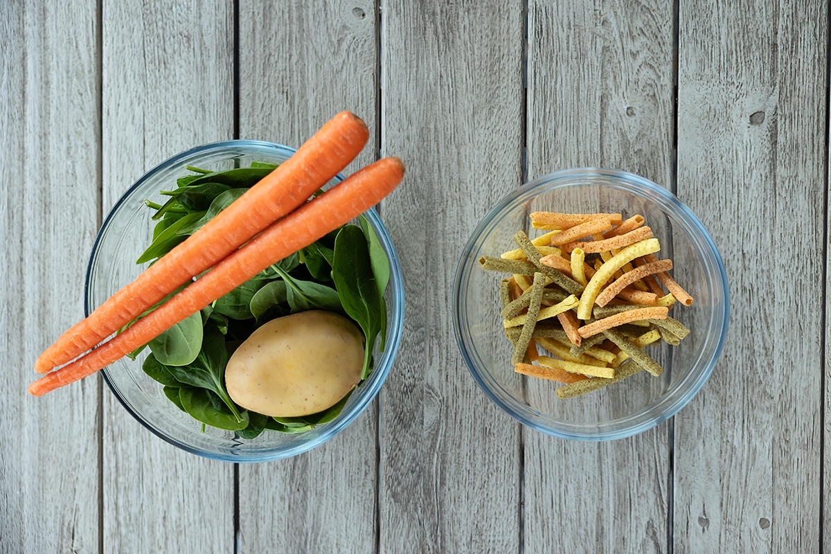 Picture of a bowl of whole vegetables next to a bowl of processed veggie straws.